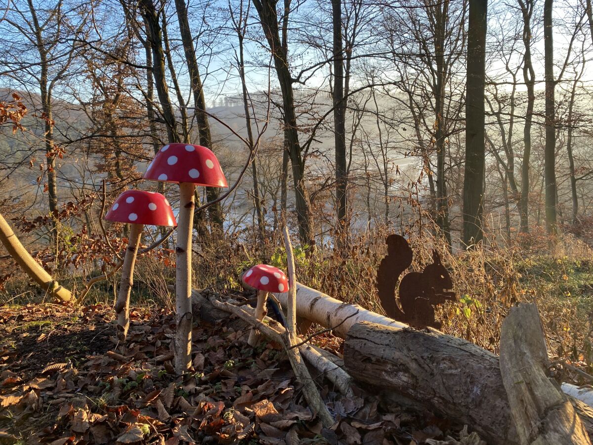 Fliegenpilze und Eichhörnchen-Figur im Herbstwald, dahinter der See